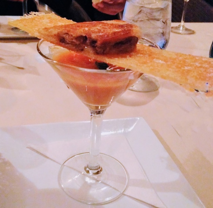 tomato soup in a martini glass with a thin stick of pressed mozzarella and a small kalua pork sandwich.