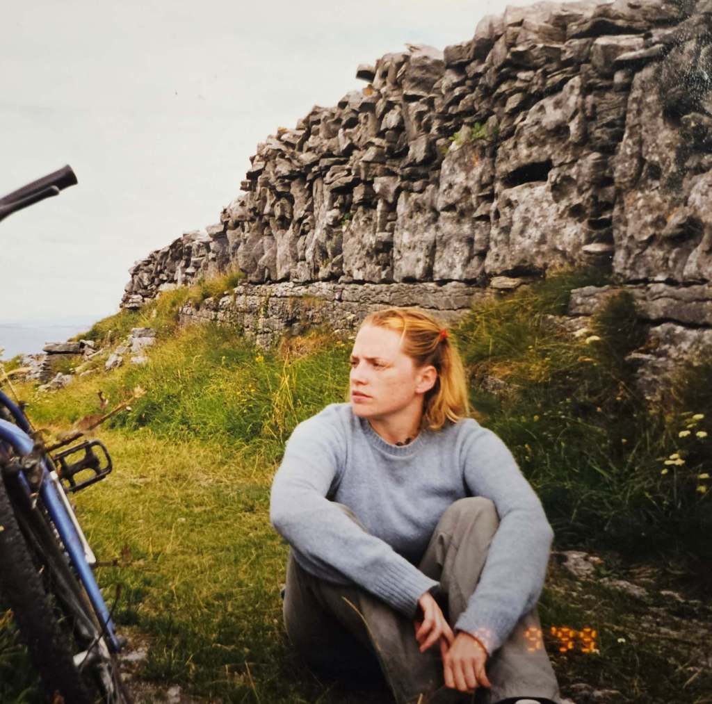 Young Adrienna sitting on a trail in the Aran Islands, Ireland, with stone walls in the back ground