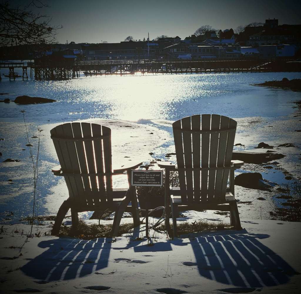 Two deck chairs facing a view of a winter harbor scene.